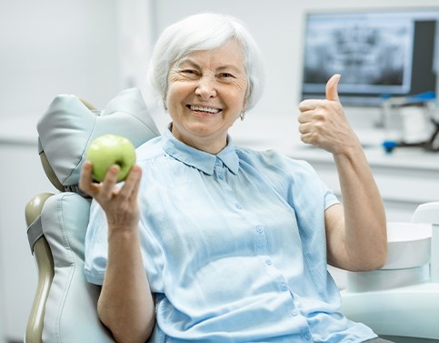 Senior woman holding an apple after all on 4 dental implant tooth replacement