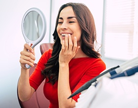 Woman smiling at reflection in handheld mirror