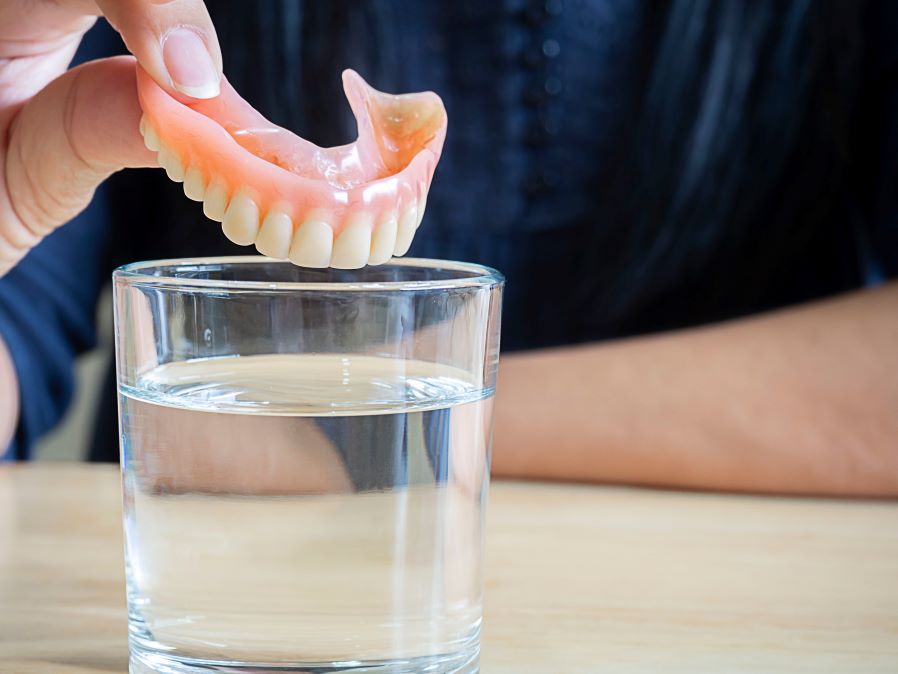 A pair of dentures being placed into a cup of water.